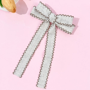 Detail of grey bow hair clip with brown scalloped edges and elegant long ribbons