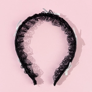 Détail d'un serre-tête en dentelle noire avec petits nœuds blancs et bordure ondulée