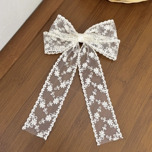 Elegant off-white lace bow hair clip with long ribbons and floral embroidery on wood