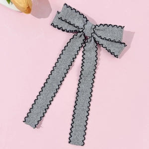 Detail of grey bow hair clip with black wavy scalloped edges and woven fabric texture
