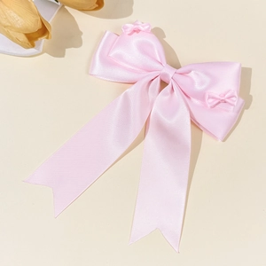 Dettaglio del fermaglio a fiocco in raso rosa con nastri lunghi e consistenza setosa