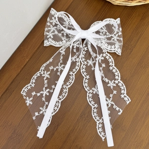 Close-up of a white lace bow hair clip with floral embroidery and satin ribbons