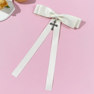 Detail of white satin bow brooch with vintage silver cross on pink background