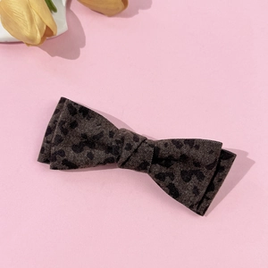 Detail of elegant leopard print bow hair clip with textured fabric on a soft pink surface