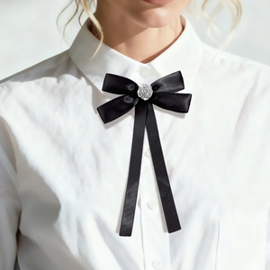 Detail showing a black satin bow tie brooch with a silver rose on a white shirt collar