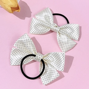 Close-up of white satin bow hair ties with black polka dots on a pink background