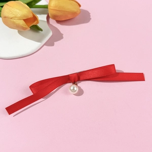 Détail de la broche nœud en satin rouge avec perle blanche sur fond rose