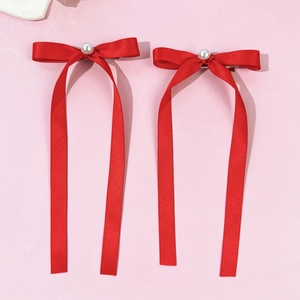 Détail de barrettes nœuds rouges avec perles et longs rubans sur fond rose tendre