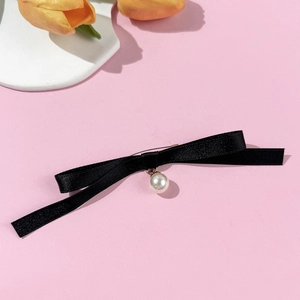 Détail d'une élégante broche nœud en satin noir avec pendentif perle blanche sur fond rose