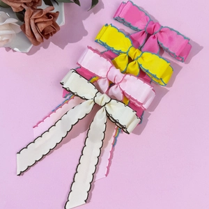 Quatre barrettes à nœud en ruban gros-grain coloré avec surpiqûres sur fond rose doux