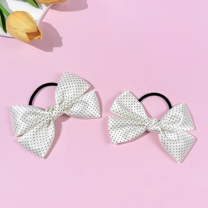 Close-up of white satin bow hair ties with black polka dots on a pink backdrop