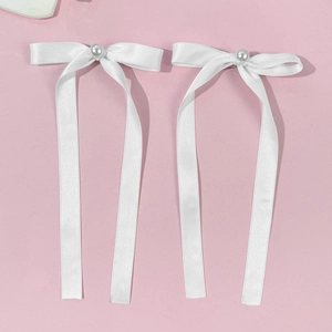 Détail de barrettes à nœuds en satin blanc avec perle centrale sur fond rose