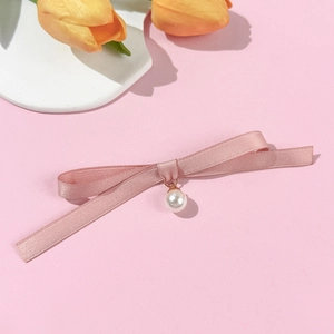 Détail d'une broche nœud en satin rose avec pendentif perle sur fond rose élégant