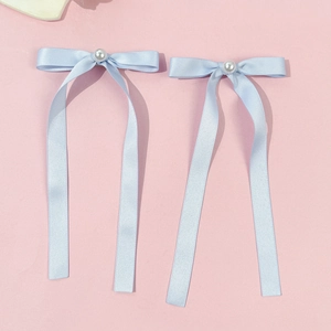Paire de barrettes à nœuds en satin bleu clair avec perles sur fond rose pastel