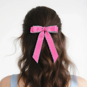 Détail d'une pince à cheveux nœud rose avec bordure ondulée verte sur cheveux bruns