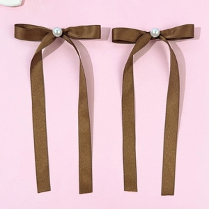 Vue détaillée de nœuds de cheveux en satin marron avec perles sur fond rose pastel