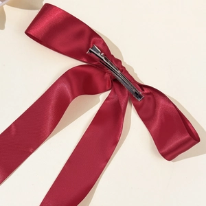 Detail of a large dark red satin bow hair clip with long ribbons and a silver metal alligator clip