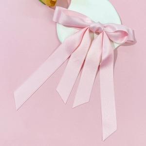 Dettaglio fermaglio per capelli con fiocco in raso rosa e nastri lunghi su cuore