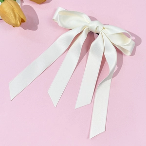 Dettaglio del fiocco in raso bianco crema con nastri lunghi su sfondo rosa chiaro