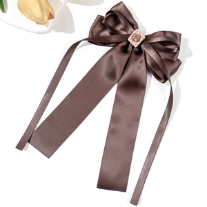 Detail of coffee brown satin bow hair clip with cute bear cookie charm on white background