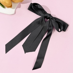 Dettaglio dell'elegante fiocco di raso nero con lunghi nastri fluidi su sfondo rosa chiaro