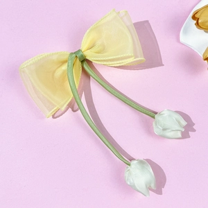 Detail van gele organza strik haarklem met groene linten en witte tulp-hangers