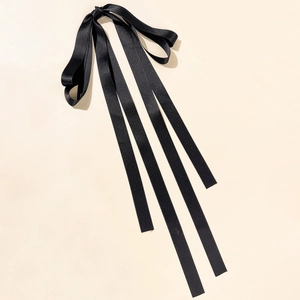 Dettaglio ravvicinato del fiocco in raso nero con nastri su sfondo beige in stile minimalista