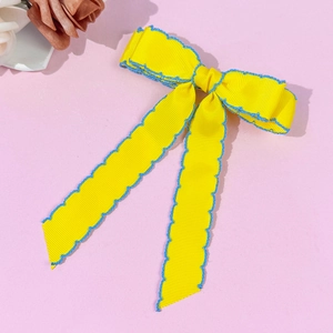 Barrette à cheveux avec nœud en ruban jaune et bordure festonnée bleue sur fond rose