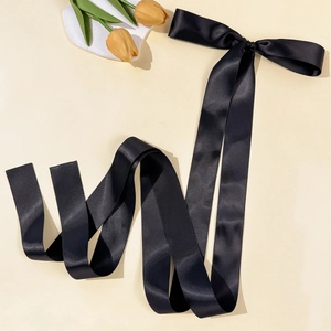 Close-up of elegant long black satin ribbon hair clip with bow on warm beige background