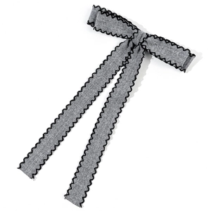 Close-up of grey ribbon bow hair clip with black scalloped edges and textured fabric detail