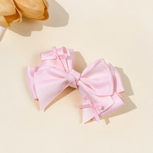 Detail of layered light pink satin bow hair clip with small side bows on cream background