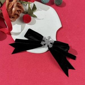 Detail view of a black velvet Christmas bow hair clip with silver snowflake on red backdrop