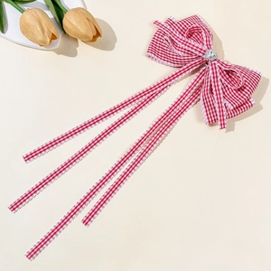Détail d'une barrette à nœud à carreaux rouge et blanc avec strass cœur et rubans