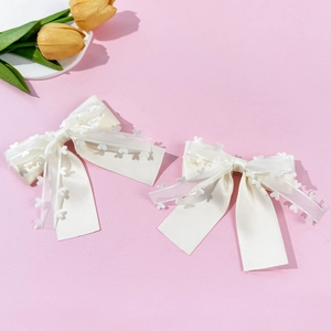 Détail de barrettes nœuds blanc crème avec dentelle à cœurs sur fond rose doux
