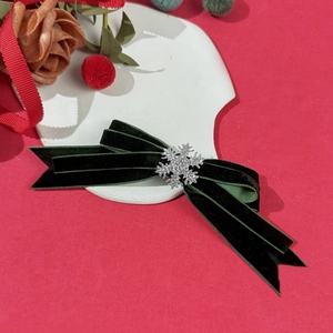 Close-up of dark green velvet bow hair clip with silver snowflake detail on festive background