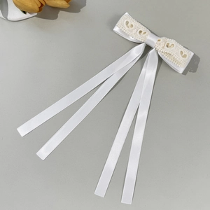 Detail of elegant white satin bow hair clip with lace trim and long flowing ribbons
