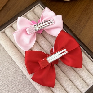 Pink and red satin bow hair clips with metal alligator clips on display box