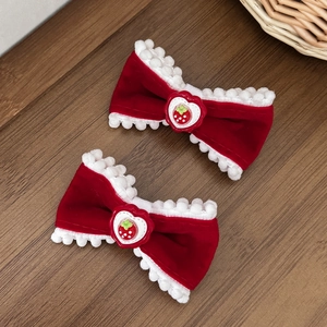 Detail of red velvet bow hair clips with white pom-poms and strawberry heart centers