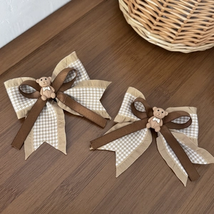 Détail de barrettes nœuds ourson avec motif pied-de-poule et rubans bruns sur bois