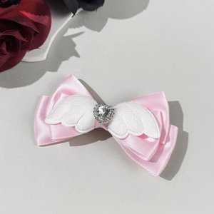Detail van roze satijnen haarclip met witte pluchen vleugels en hartvormige strass in het midden