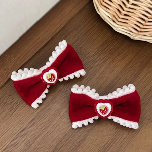 Detail of red velvet bow hair clips with white pom-pom trim and strawberry heart centers