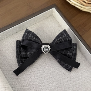 Detailed close-up of houndstooth and satin bow hair clip with a rhinestone heart centerpiece