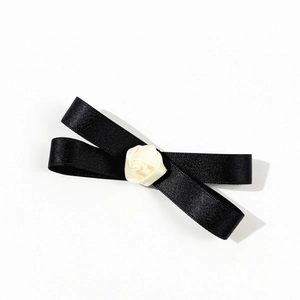 Détail d'un nœud en satin noir avec une rose en tissu crème pour accessoire scolaire