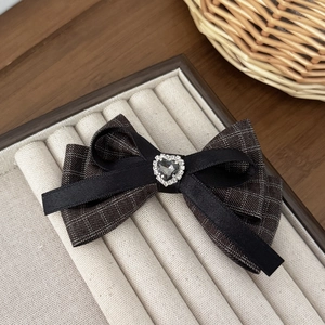 Detail of tweed houndstooth bow hair clip featuring a rhinestone heart center on beige tray
