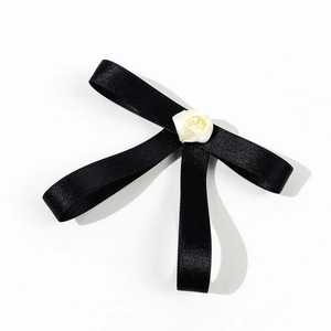 Détail d'un nœud en ruban noir avec une petite rose en tissu blanc au centre