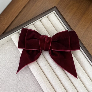 Close-up of a burgundy velvet double-layered bow hair clip on a soft display tray
