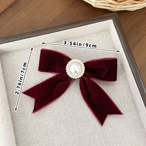 Detail of burgundy velvet bow hair clip with central pearl and vintage gold accents
