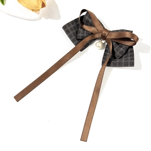 Detailed close-up of a plaid bow hair clip featuring a brown ribbon and pearl pendant