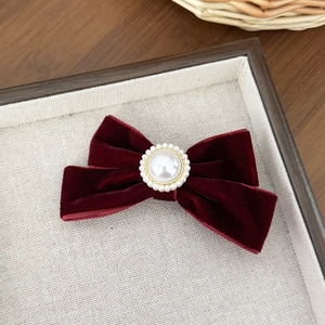 Detailed view of the burgundy velvet bow hair clip with central pearl on a beige tray