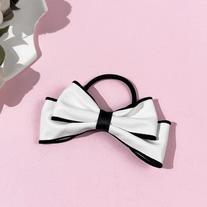 Detail of elegant black and white faux leather bow hair tie on a soft pink background